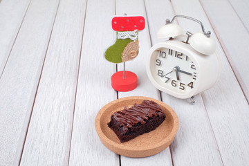 Alarm clock, note clipper and  chocolate brownie with melted chocolate on a wooden plate