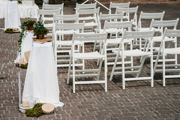 Wooden white chairs are decorated with ribbons and greens in the backyard banquet area. Wedding ceremony. road. wedding decor. Side view and rear view.