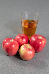 Group of red ripe apples in front of a glass full of apple juice