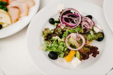 Gourmet salad in a white plate. Slices of cheese, lettuce. White plate on white table. Food. Holiday. flat lay. top view.