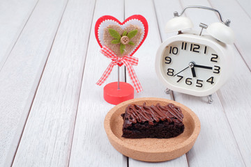 Alarm clock, note clipper and  chocolate brownie with melted chocolate on a wooden plate