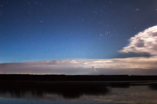 Clouds and stars above lake in the summer night before thunder