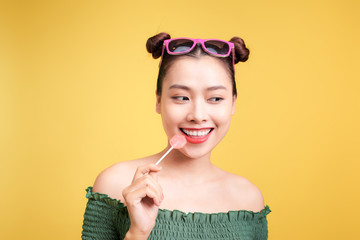 Glamor stylish beautiful young woman model with red lips holding candy on yellow background.