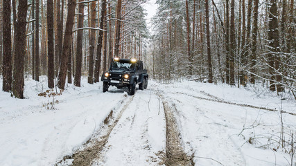View on SUV 6x6 that rides by winter road in snow-covered forest