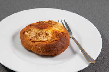 Single small bun beside a silver small fork on a white plate