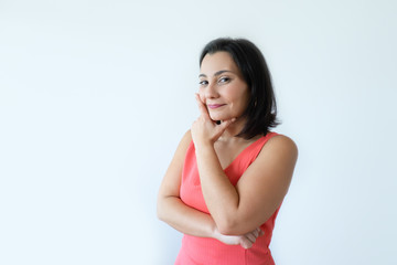 Portrait of positive attractive Caucasian woman touching chin and smiling. Pretty middle aged woman in pink dress thinking about new project. Happy planning concept.