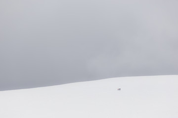 A very minimalistic view of two distant people over a mountain covered by snow
