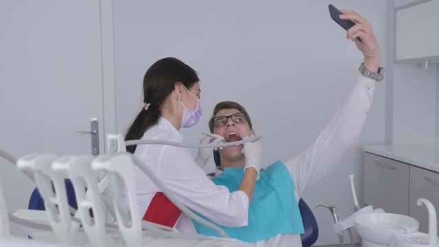 A patient sitting in a dental chair during dental treatment takes a picture of himself with a smartphone.