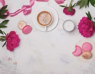Coffee, pink peonies and macarons on the marble table