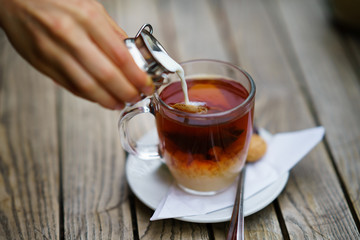 Pouring milk in tea in glass cup on wooden table