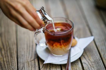 Pouring milk in tea in glass cup on wooden table