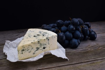 Blue cheese/Roquefort with fresh grape on white paper. Fruits, cheese, top view. Delicacy food.