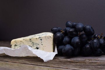 Blue cheese/Roquefort with fresh grape on white paper. Fruits, cheese, top view. Delicacy food.