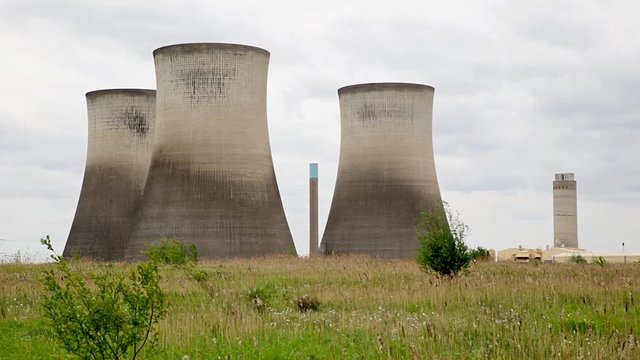 Concrete cooling towers and chimneys of power station across grass meadow