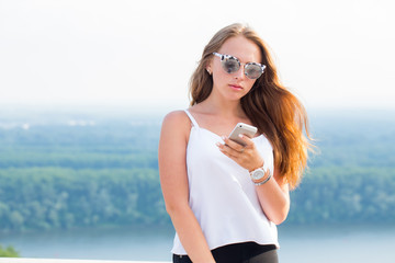 Beautiful student girl uses a smartphone on nature