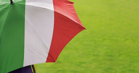 Italy flag umbrella. Close up of printed umbrella over green grass lawn / field. Rainy weather...