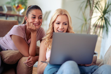 Two happy female friends using laptop