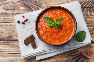 Tomato soup in a wooden bowl with pieces of toast on a rustic table.