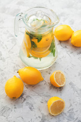 Lemonade in a transparent jug. Lemons, mint, glasses, decanter on a concrete background