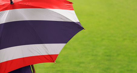 Thailand flag umbrella. Close up of printed umbrella over green grass lawn / field. Rainy weather forecast concept.	