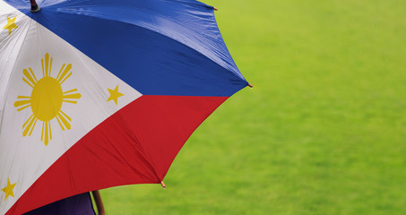 Philippines flag umbrella. Close up of printed umbrella over green grass lawn / field. Rainy weather forecast concept.	