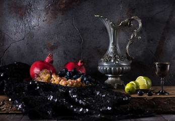 Still life with a jug of wine, grapes  and pomegranates on a dark concrete background © Rozmarina