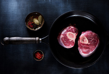 Osso buco raw steaks in a cast-iron pan, herbs and spices, top view
