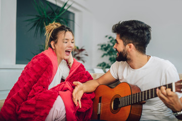 Young couple are playing guitar and happy smiling while sitting on couch at home