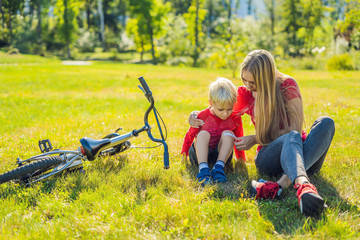 The boy fell off the bicycle, his mother pastes a plaster on his knee