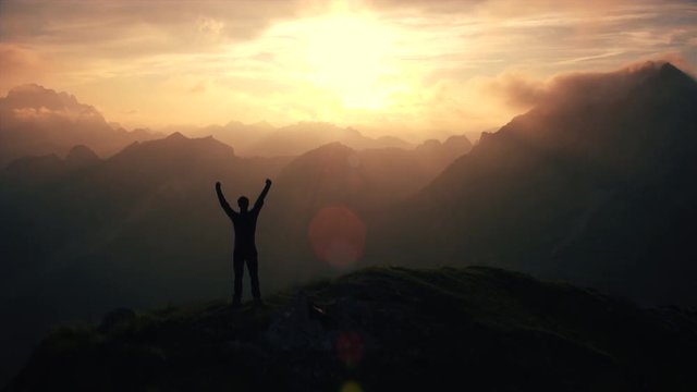 Aerial, edited - Triumphant hiker standing on top of the mountain raising arms