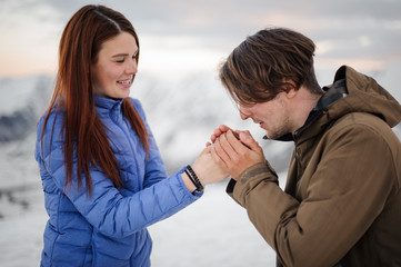 Young man warming his girl hands with breathing in mountains