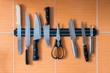 Knives hang on a magnet holder. Orange kitchen wall