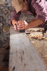 Carpenter smoothing out long wooden beam with tool