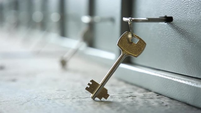 The keys inserted into keyholes of safes. Keys are inserted into keyholes of safes. One key is inserted, another is suspended in a ring. Light safes. It is removed through refocus.