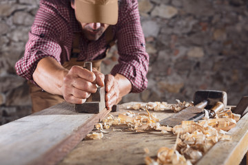 Carpenter smoothing out long wooden beam with tool