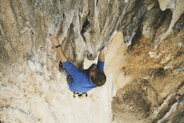 Young man looking up while climbing challenging route on cliff.