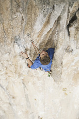 Young man looking up while climbing challenging route on cliff.