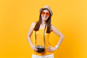 Happy traveler tourist woman in summer casual clothes, hat with retro vintage photo camera isolated on yellow orange background. Girl traveling abroad travel on weekends getaway. Air flight concept.