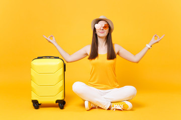 Traveler tourist woman in summer hat sit with suitcase crossed legs, meditate spread hands, isolated on yellow orange background. Passenger traveling abroad on weekends getaway. Air flight concept.