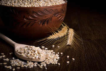 Fototapeta na wymiar Pearl barley in a wooden bowl on a wooden background near the ears of wheat. wooden spoon with pearl barley