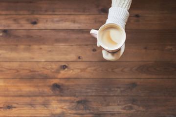 A girl in the winter knitted mittens with an cup of coffee on the wooden table background. Winter concept