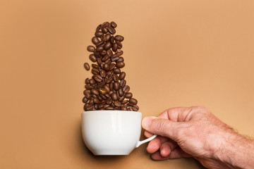 Mano de hombre sosteniendo una taza de café blanca con sabrosos granos de café sobre un fondo marrón liso y aislado. Vista superior. Copy space
