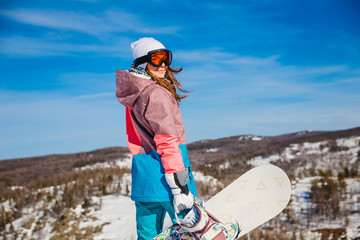 a woman with snowboarding stands high in the mountains in winter