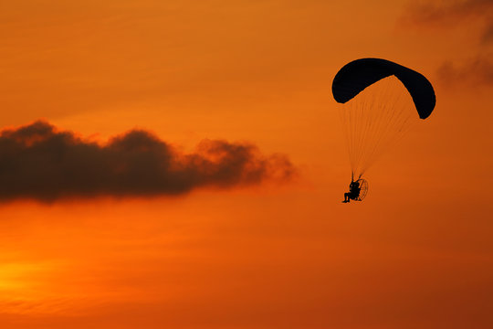 Silhouette of paramotor flying at during the sunset
