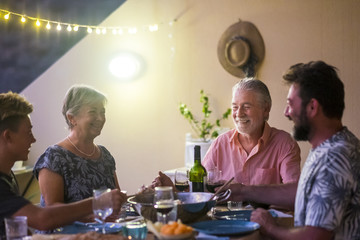 happy family with different ages from grandfathers to son and grandson all together having dinner by night in the terrace at home for nice leisure activity in love and friendship eating food and drink