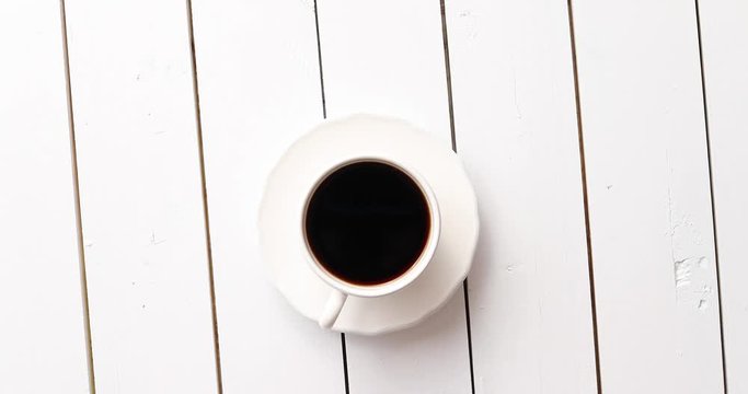 From above shot of cup of fresh hot drink standing on surface of white wooden tabletop