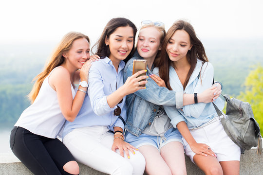 Four beautiful young women using smartphone and smiling in the Park, outdoor - Powered by Adobe