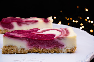 DELICIOUS HOMEMADE CHEESECAKE WITH WINTER FOREST FRUITS AND CHRISTMAS LIGHTS LIKE BACKGROUND.