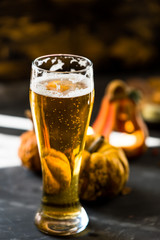 glass of golden beer on dark, wooden table, surrounded by autumn decorations, pumpkins, leaves