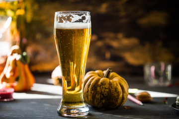 glass of golden beer on dark, wooden table, surrounded by autumn decorations, pumpkins, leaves